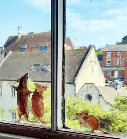 mouse family decals stuck on a window overlooking an old cotswold building and fir trees