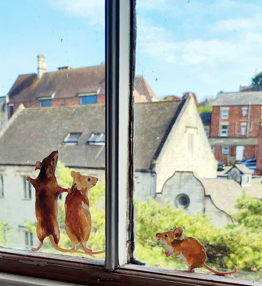 mouse family decals stuck on a window overlooking an old cotswold building and fir trees
