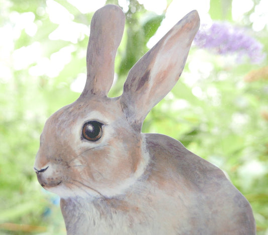 Close-up of a rabbit decal on a window with a blurred green and purple background