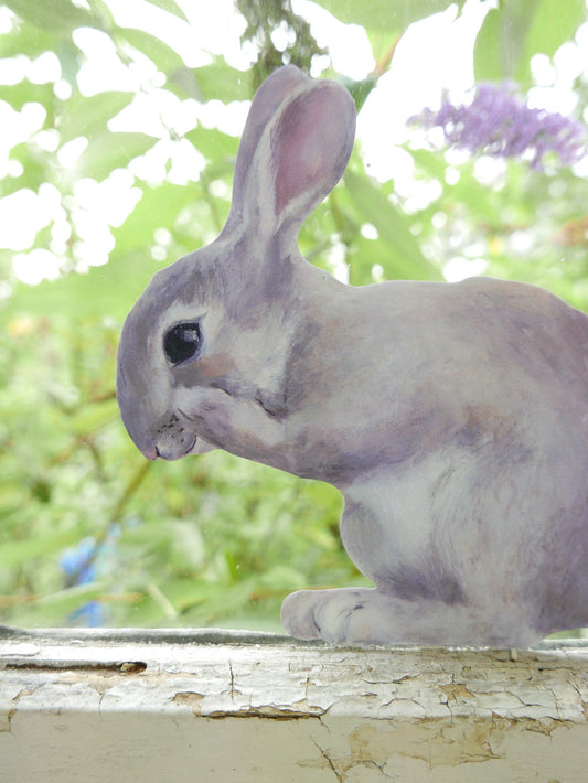 Gray rabbit decal sitting on a windowsill with a blurred green and purple background