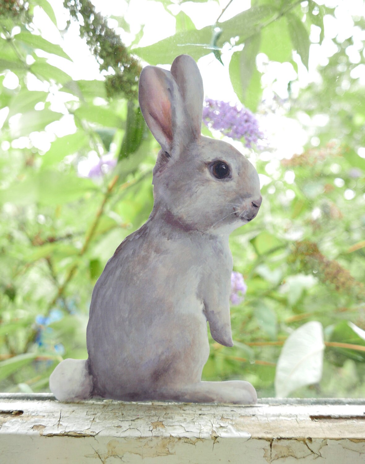 Gray rabbit decal on a window ledge with green foliage in the background