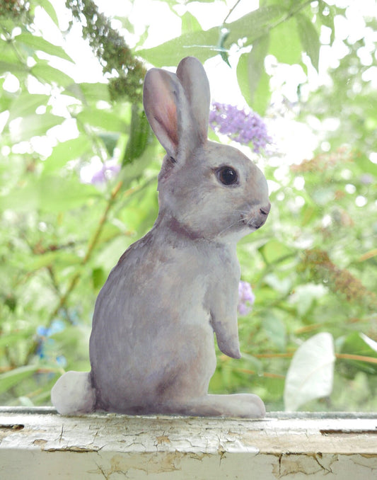 Gray rabbit decal on a window ledge with green foliage in the background