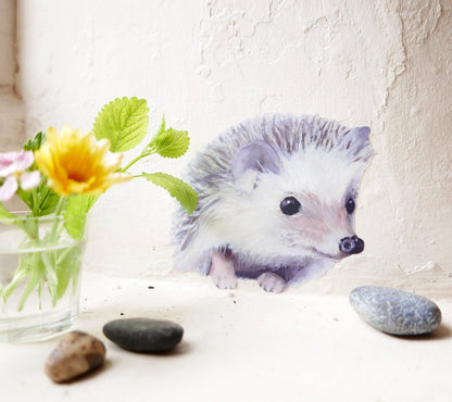 Small hedgehog sitting on a light surface with flowers and stones in the background