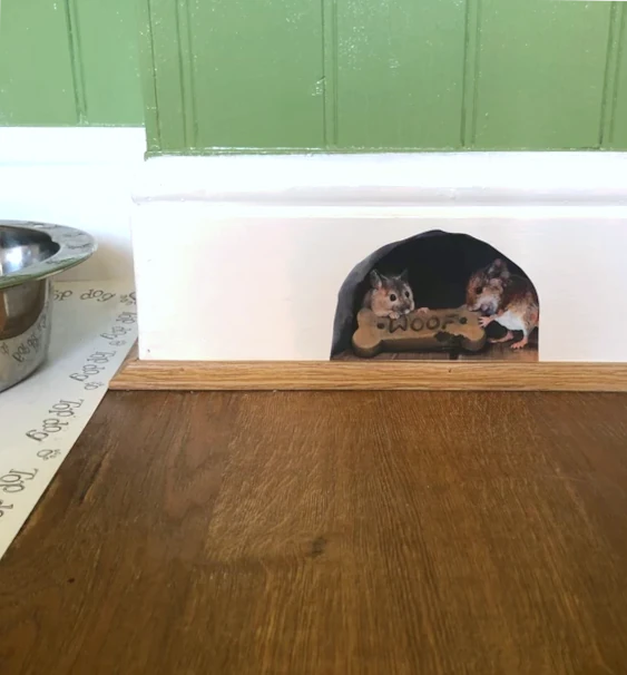 decal on a skirting board next to dog bowl featuring 2 mice eating a dog biscuit in a mouse hole