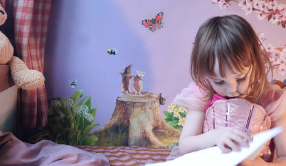 Child reading a book in a cozy room with a teddy bear, plants, and a colourful nature garden themed fabric wall mural