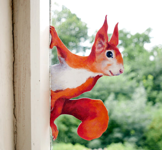 Decorative squirrel sticker on a window with a blurred green outdoor background