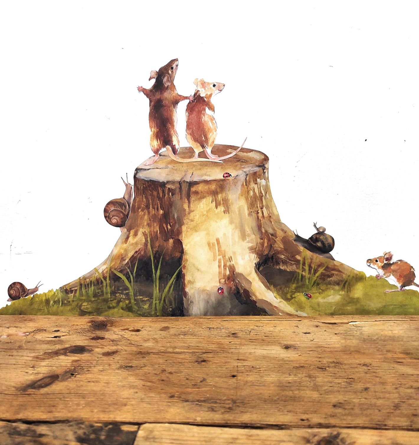 fabric wall decals of a tree stump, mice, snails and laybirds on a white wall with a wooden floor in the foreground.