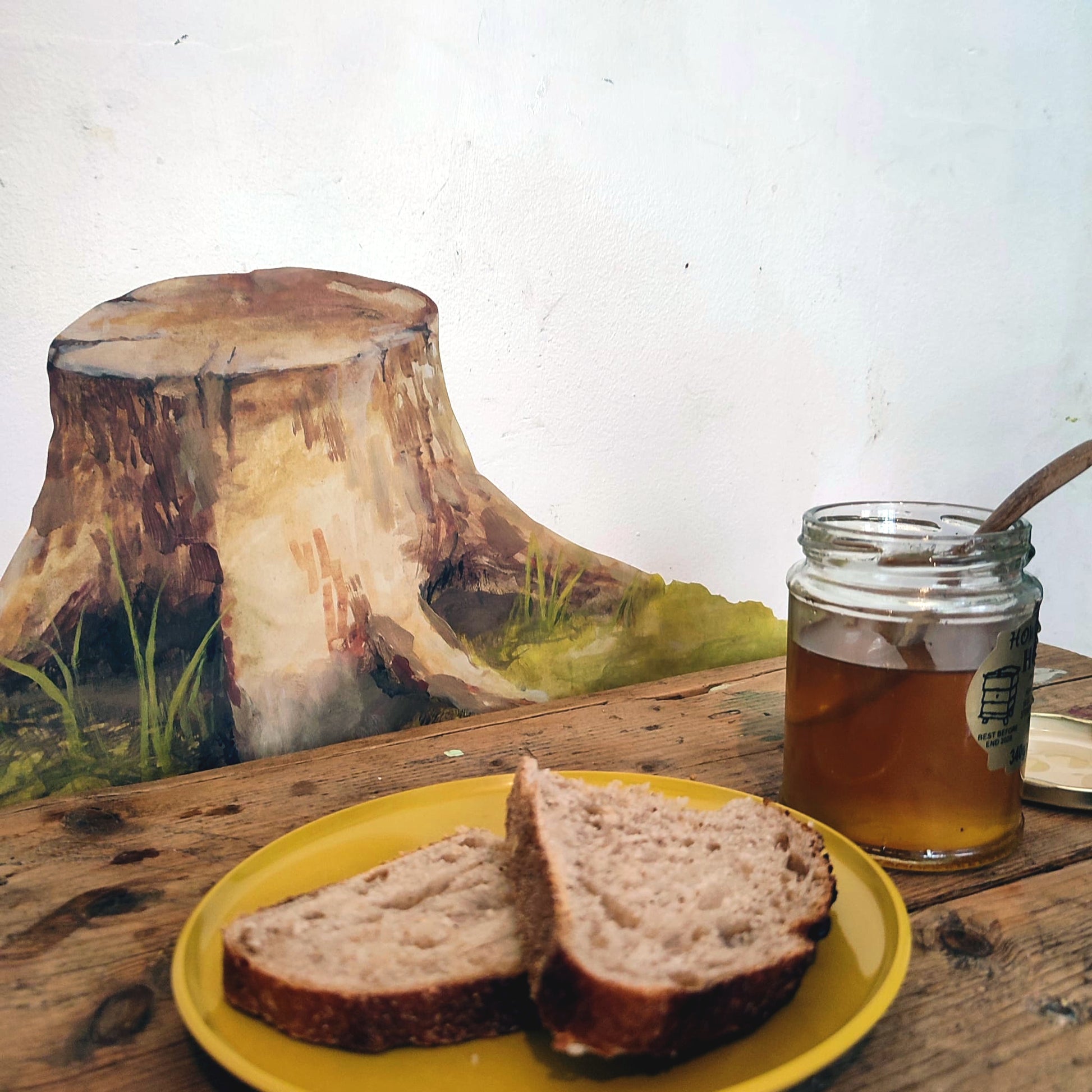 a tree stump decal on a white wall behind a table with bread and honey in the foreground