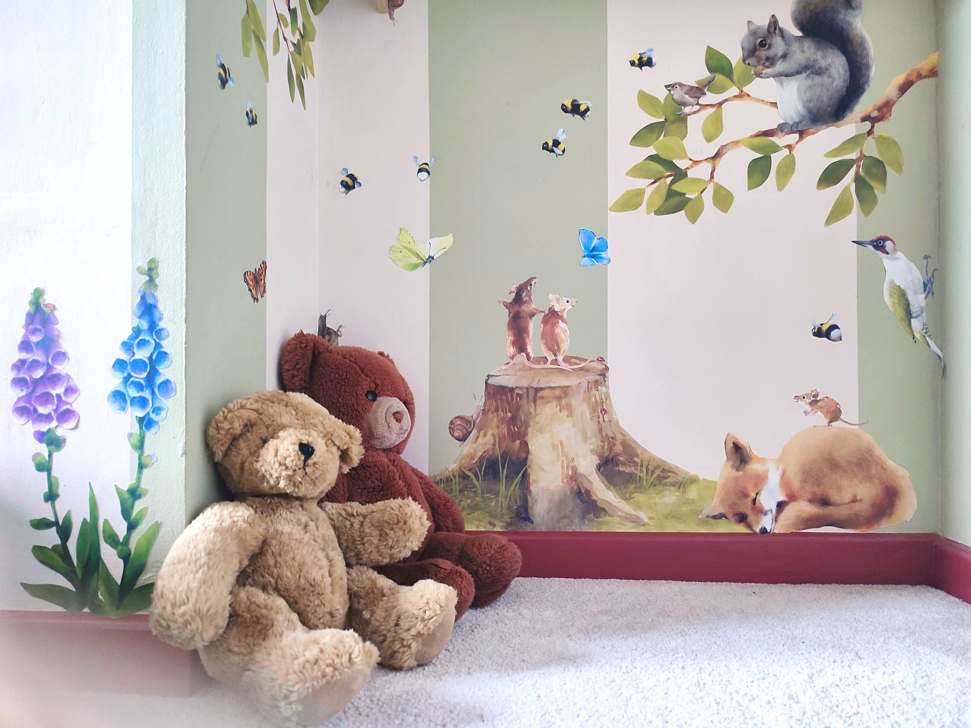 Two teddy bears sitting on a floor with woodland-themed fabric wall decals in the background.